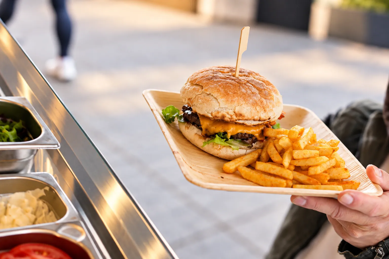 Burger mit Pommes wird bei Sonnenschein an der Foodtruck-Theke ausgegeben