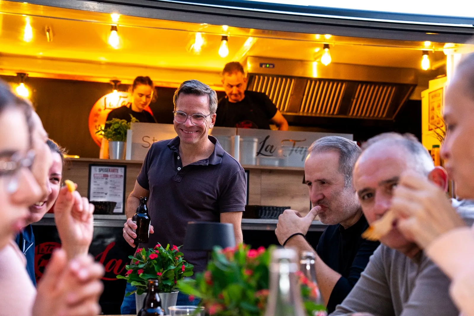 Gäste feiern am Stehtisch vor dem Foodtrailer unter einer Lichterkette