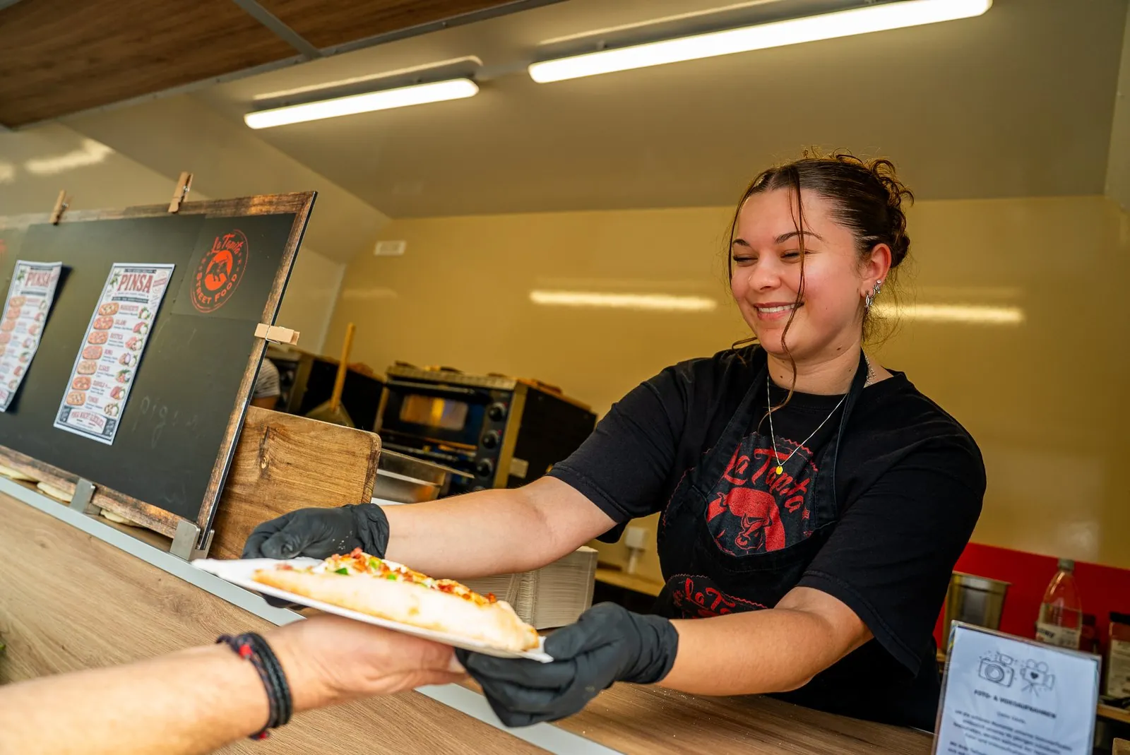 Mitarbeiterin gibt am Foodtruck Pinsa aus, daneben die Pinsa-Tafel