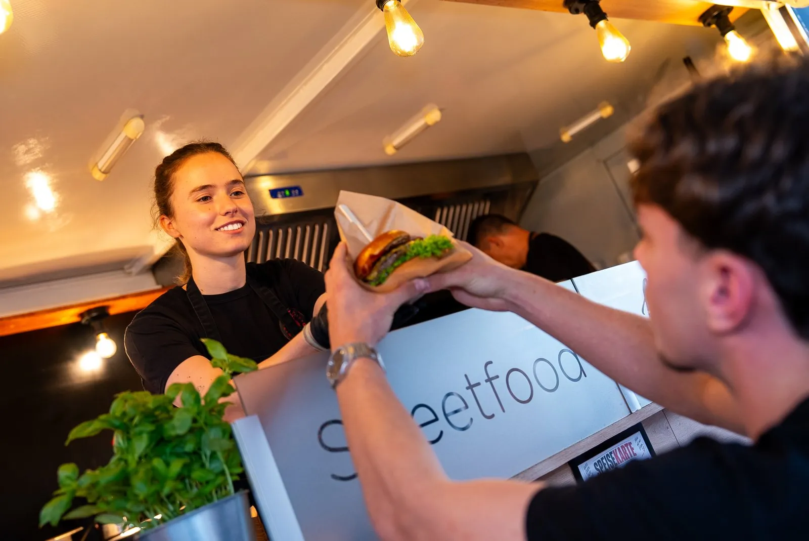 Mitarbeiterin reicht einen Burger über die Theke des Foodtrailers