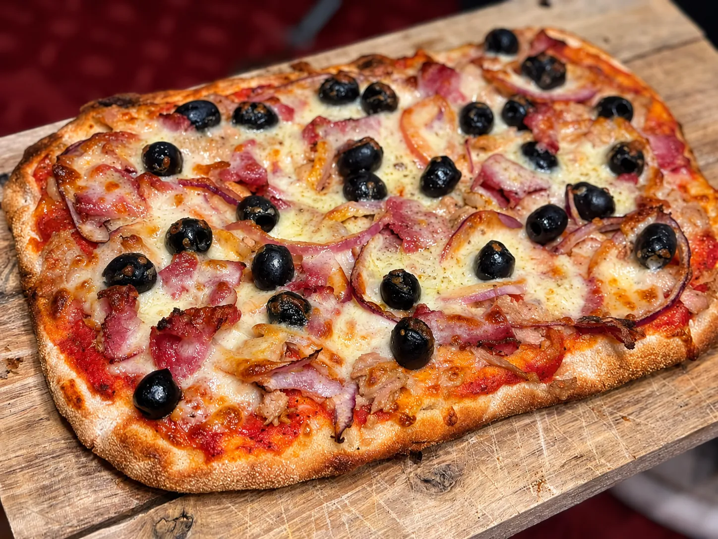 Pinsa mit Schinken und Oliven auf einem Holzbrett